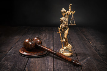 Judges gavel and Themis on a wooden table top, dark background. The concept of justice and dealing with court cases. Citizens' problems in courts. Symbols of judge and courts. Sense of justice.