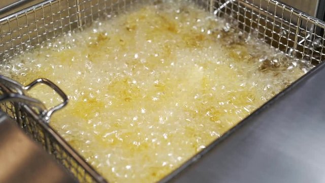 Slow Motion of boiling goldend french fries in bubbly hot cooking oil. Submerging golden french fries in deep fryer with hot cooking oil.