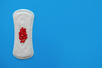 Menstrual pad with red sequins on a blue background, top view, miniature of the menstrual period,...