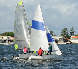 Children close racing small sailboats  on a coastal lake.