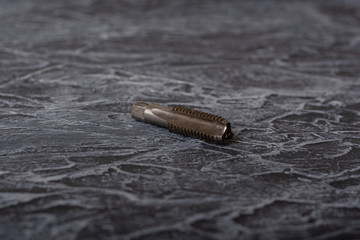 Tap - a tool for cutting internal threads, is a screw with cut straight or helical chip grooves that form cutting edges. There is some rust and metal shavings. lies on a concrete surface