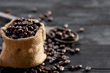 Roasted coffee beans are placed in a small sack, placed on a black wooden table.