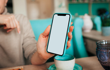 woman's hand with a French manicure holds a mint and black phone against the background of a table in a cafe with blue porcelain cups. Business meeting in a restaurant, coworking for freelancers.