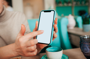 woman's hand with a French manicure holds a mint and black phone against the background of a table in a cafe with blue porcelain cups. Business meeting in a restaurant, coworking for freelancers.