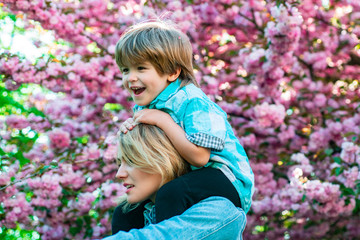 Mother and child girl playing and hugging. Portrait of happy mother giving son piggyback ride on his shoulders and looking up.