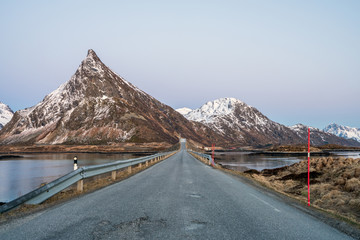 Road towards steep mountain formation in Fredvang, Lofoten, Norway at blue hour. Peaks covered with snow during road trip in spring. Traveling and explore concept.