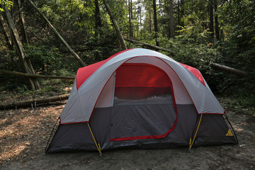 A red and gray tent setup in the woods.