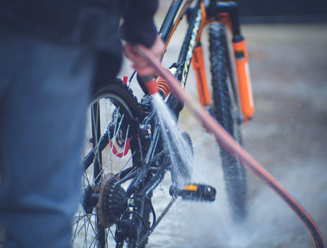 Man washing sport bike with a strong jet of water after a ride in forest. Soft focus image of hand with a water hose in the yard.