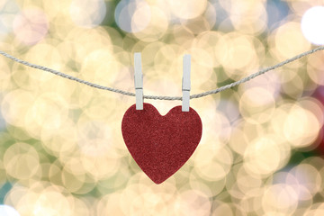 Red heart hanging on a hemp rope on the gold bokeh background.