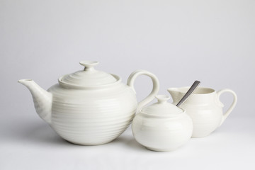 a white ceramic teapot sugar and cream set on a wooden table top