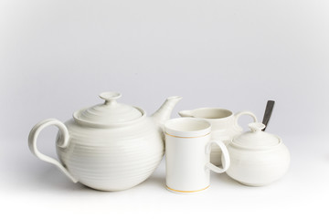 a white ceramic teapot sugar and cream set on a wooden table top