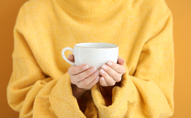Beautiful young woman in warm sweater and with hot tea on color background, closeup