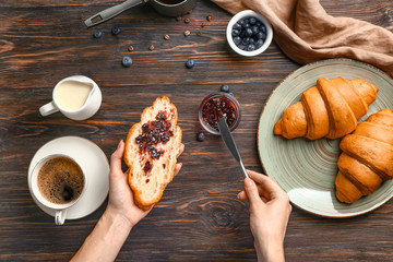 Woman spreading jam onto fresh croissant, top view