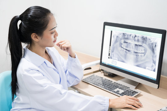 Portrait Asian woman dentist sitting and looking tooth image x-ray in computer.Female doctor examining patient tooth with panoramic radiograph on dental chair at the dental office.