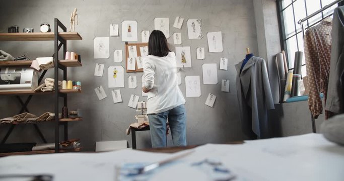 A clothes designers is looking at her sketches while in the office, working on her new fashionable clothes collection - fashion, success concet 4k footage
