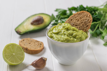 Guacamole with bread, lime, garlic and parsley on a white wooden table. Diet vegetarian Mexican food avocado.