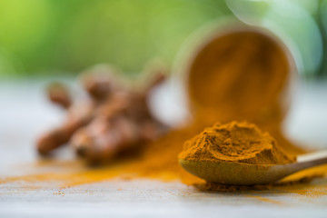 Turmeric powder and fresh turmeric in wood bowls on wooden table.