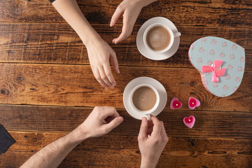 Obraz premium Valentine's Day celebration concept. A nice gift for your loved one. Hands of man and woman with coffee mugs on a wooden table background. Copy space. Flat lay. Close-up.