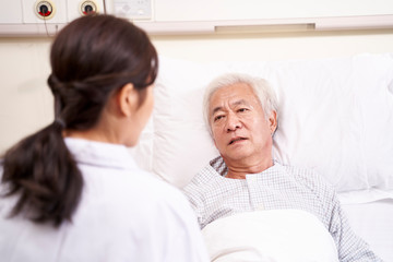 young asian doctor talking to senior patient at bedside in hosptial ward