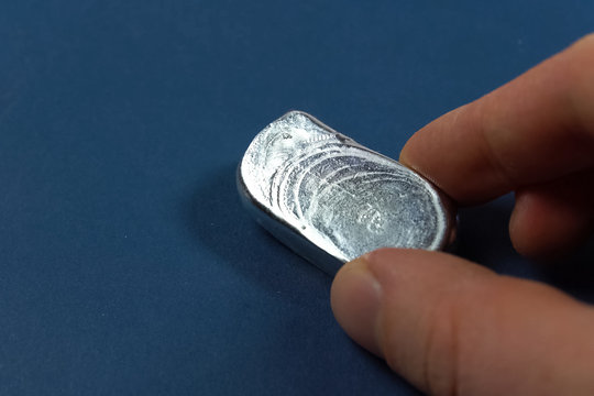 A Bar Of Aluminum In His Hand. Spilled Aluminum Ingot.