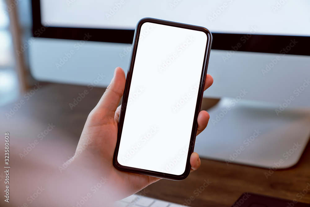 Wall mural woman holding smartphone mockup of blank screen and computer on the table office. take your screen t