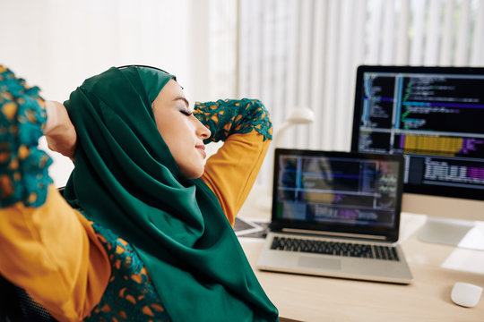 Young muslim woman stretching in her chair after working on programming code