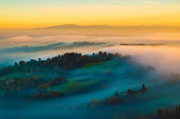 Fototapeta premium Tuscany hilly, foggy, sunset scenery; as seen from one of the towers in San Gimignano, Italy.