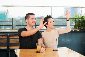Smiling young people sitting at cafe table with cocktails and waving with hands when trying to attract attention of waiter or friend
