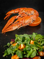 Vertical shot of boiled crawfish and salad with orange and herbs on a cutting board black stone on a dark background. Food porn tasty concept
