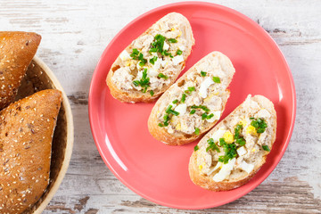 Slice of baguette with fish paste on plate and fresh rolls in wicker basket