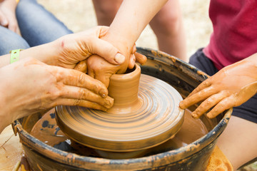 A close up view on ceramic production process on potter's wheel with children. Clay crafts with kids concept.