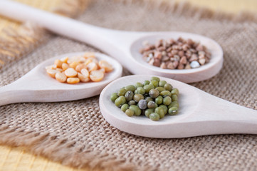 Three wooden spoons with cereals buckwheat, mung beans and peas on burlap on the table