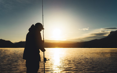 silhouette fisherman wirh fishing rod at sunrise sunlight, outline man enjoy hobby sport on evening lake, person catch fish background night sky, relaxation fishery concept - obrazy, fototapety, plakaty