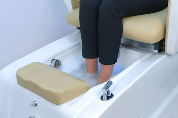 Woman is soaking feet in bath spa salon sitting in pedicure chair, legs closeup. Legs of woman...