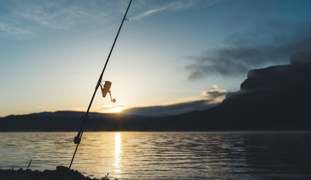 fishery concept, outline fishing rod at sunrise sunlight, hobby sport on mist evening lake, catch fish on river on background night sky foggy mount