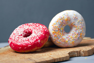 sweet multi-colored. assorted donuts with icing and powder on a wooden board on gray background.