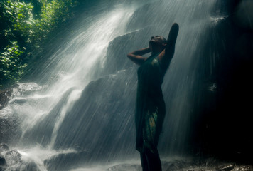 Obraz premium young attractive and blissful Asian Indonesian woman overwhelmed by the beauty and purity of natural waterfall in tropical jungle enjoying happy the amazing and exotic trip