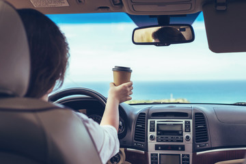 Woman driver drinking coffee paper cup inside car during driving. Girl relaxing in auto trip...