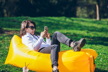 young pretty woman on yellow inflatable mattress in city park surfing in phone