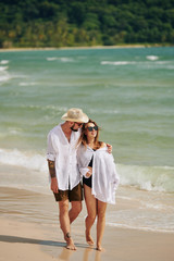 Young man hugging his girlfriend when they are walking on beach together on summer day