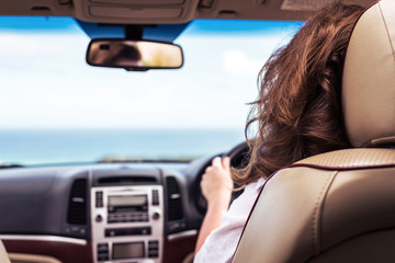 Plakat Woman driving a car relaxing in auto trip traveling along ocean tropical beach in background. Traveler concept. Back view