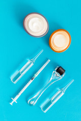 Dermatologist work desk with tools. Dermaroller, syringe, ampoule on blue background top-down flat lay