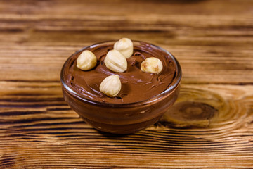 Glass bowl with chocolate spread and hazelnuts on a wooden table