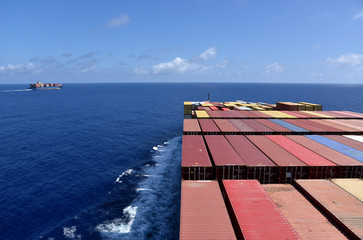 Cargo container ship sailing through calm  blue ocean, view on deck loaded with boxes. 