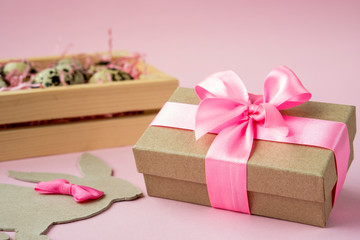 Easter eggs in a wooden box on a pink background. Easter Bunny with a pink bow. Easter gift with...