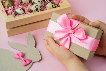 Easter eggs in a wooden box. Hands holding an Easter gift on a pink background. Easter Bunny with a...