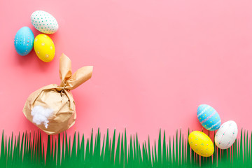 Easter symbols. Bunny and painted eggs on grass on pink background top-down frame copy space