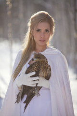A beautiful girl in a white coat walks in the forest. The huntress with a bird in her hands.