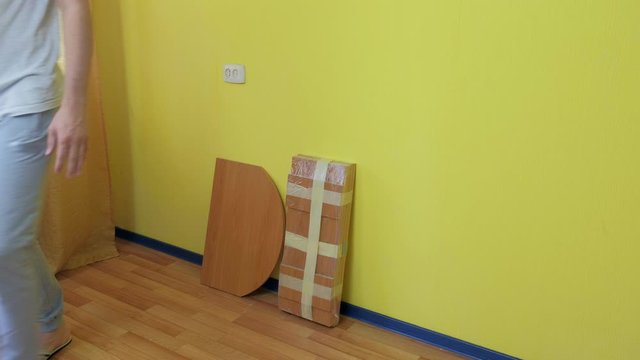 Unrecognizable man brings parts of furniture into the room to start assembling the computer table. Man is preparing to collect the table at home. Assembling furniture with your own hands.