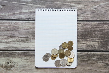 Notepad with a blank white sheet in a checker paper with russian coins lies on the background of wooden boards